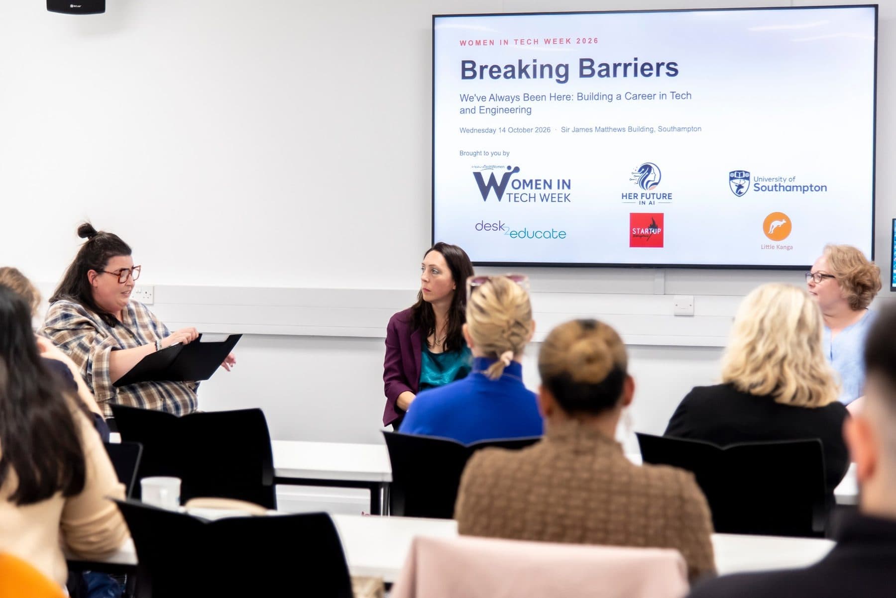 Charlie hosting the Breaking Barriers panel at Women in Tech Week 2026, with two panellists beside her and the event slide on screen